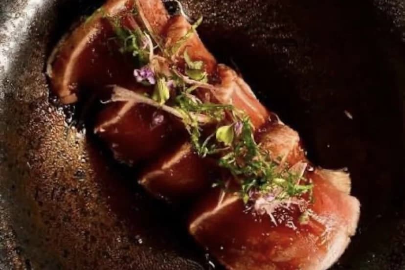 Lonchas de otoro marcadas con brotes y flores comestibles sobre un glaseado oscuro, la mejor marisquería de Marbella