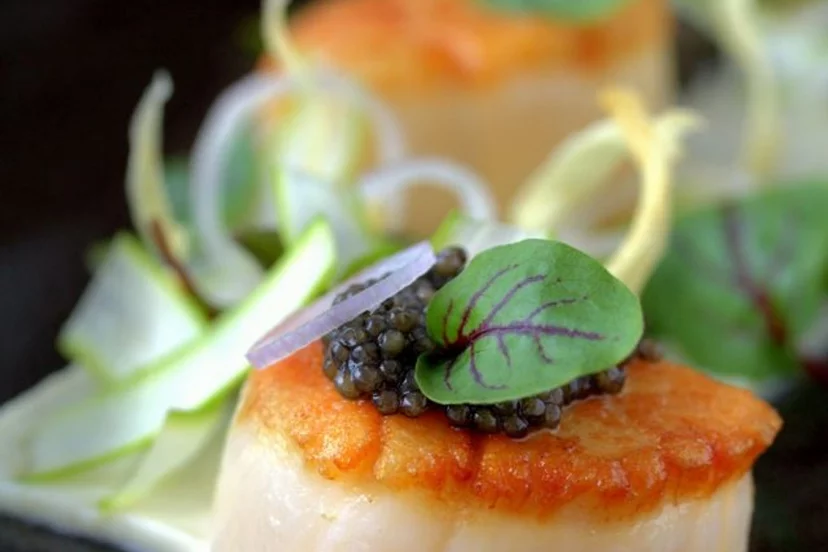 Vieira marcada coronada con caviar, un aro de cebolla morada y una hoja de nervio rojo, caviar en Puerto Banús