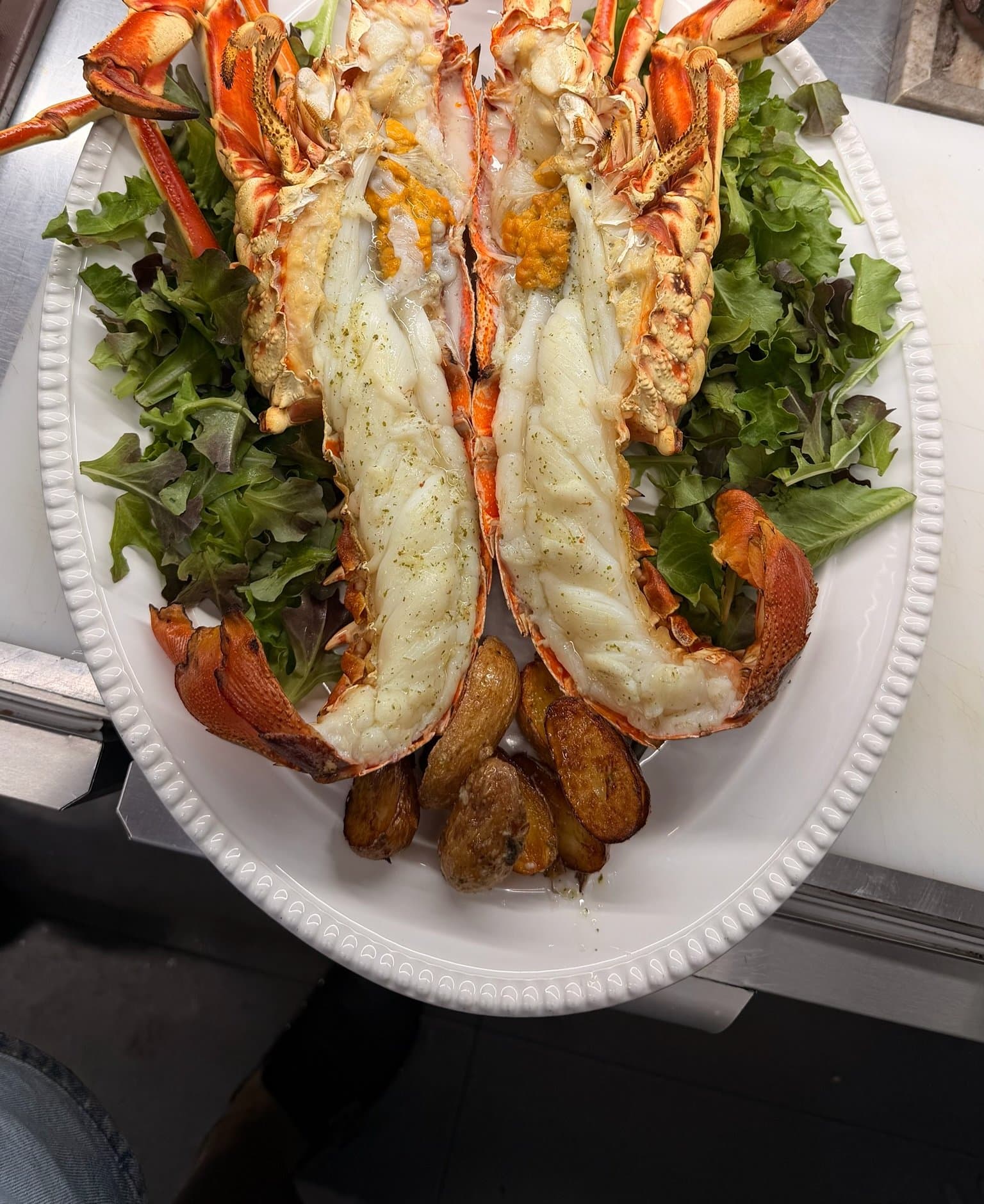 Gegrillte Languste, halbiert, mit Rucola und gerösteten Kartoffeln – ein Signature-Gericht dieses Fischrestaurants in Marbella